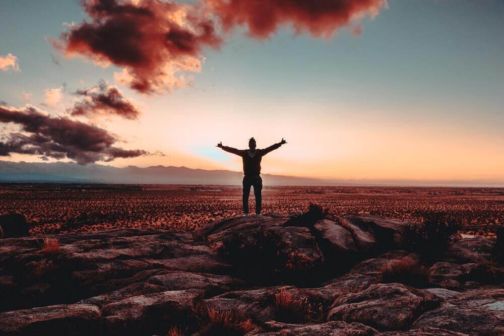 person with arms outstretched in front of sunset